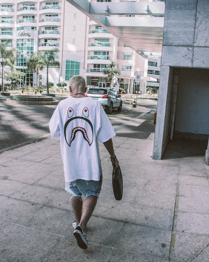 Photo of Man in a White Bathing Ape T-shirt Holding a Black Bag Walking Down the Sidewalk